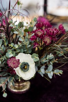 a vase filled with flowers and greenery on top of a table