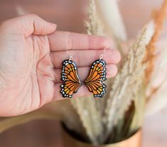 a hand holding a pair of earrings with an orange and black butterfly on the front