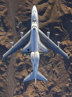 an aerial view of a jet flying over the desert area with mountains in the background