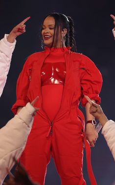 a woman in a red outfit standing on top of a stage with her hands up