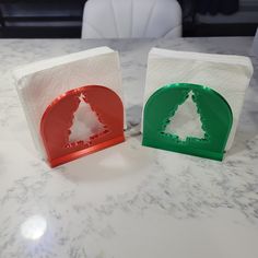 two pieces of paper with christmas trees on them sitting on a marble counter top next to each other