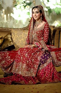 a woman in a red and gold bridal gown sitting on a couch with pillows