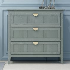 a grey dresser with two drawers and a basket on top, against a blue wall