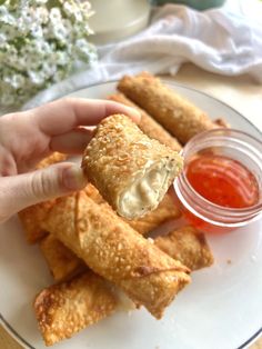 a person is holding up some food on a plate with dipping sauce in the background