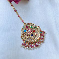 Navrattan teeka in sterling silver with 22K gold plating. It has been embellished with freshwater pearls and a mix of real and synthetic navrattan stones. The hanging beads are real rubies and freshwater pearls. Weight 13 GMs Dimensions - 2 x 1.5 inches All our Gold Plated Jewellery is made using 925 Silver as the base metal. The beads in hanging and strings (like in our 22k gold jewelry) are always precious freshwater pearls and high quality ruby, emerald and sapphire beads. The default choice 22k Gold Jewelry Necklaces, Sapphire Beads, Gold Plated Jewellery, 22k Gold Jewelry, Hanging Beads, Pearl Necklace Set, Ruby Emerald, Gold Jewelry Necklace, Emerald Necklace