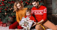 a man and woman sitting next to a little boy holding a christmas present in front of a christmas tree