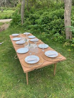 a wooden table with plates on it sitting in the grass near some trees and bushes