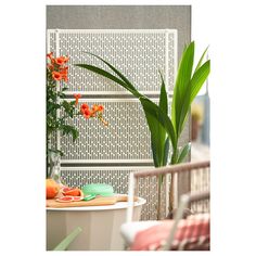 an outdoor table with flowers and fruit on it in front of a white latticed wall