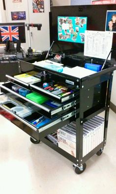 a black cart with several drawers on it in front of a computer monitor and other office equipment