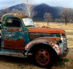 an old rusted truck sitting in a field with mountains in the backgroud