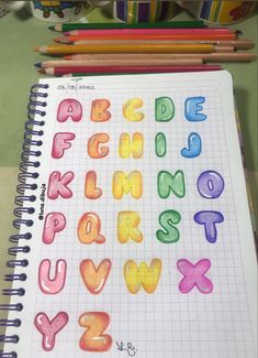 an open notebook with colorful letters and numbers drawn on it next to colored pencils