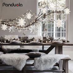 a dining room table with white flowers hanging from it's ceiling and bench in front of the window