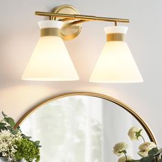 two lights are on the wall above a mirror and vase with flowers in front of it