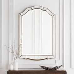 a mirror sitting on top of a wooden table next to a vase with flowers in it