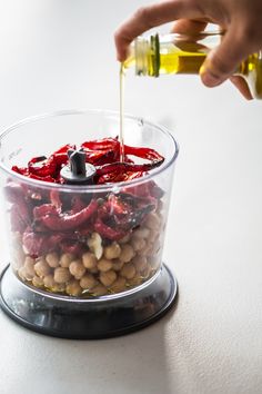 someone pouring olives into a container filled with beans and other ingredients to make an appetizer