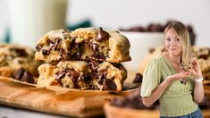 a woman standing in front of chocolate chip cookies with a glass of milk behind her