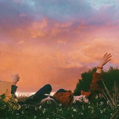 two people laying in the grass with their hands up to the sky and one person reaching for something