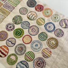 several different colored circles on a white table cloth with an embroidered design in the middle