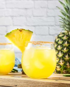 two glasses filled with pineapple margaritas on top of a wooden table next to a pineapple