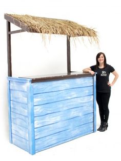 a woman standing next to a blue wooden bar with a thatch roof on top