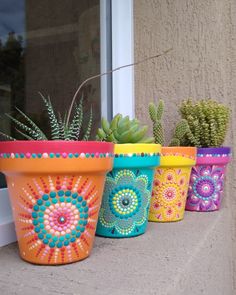 four colorful flower pots with succulents in them sitting on a window sill