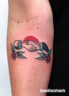 two hands touching each other with flowers and leaves around them on the left arm tattoo