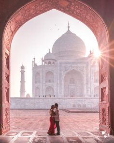 two people standing in front of an arch with the sun shining on them and one person kissing