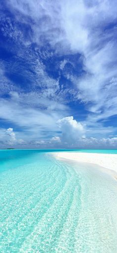 the water is very clear and blue with some clouds in the sky above it on an island