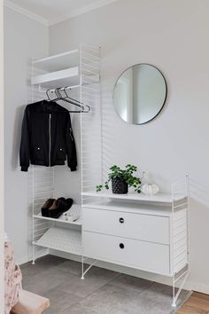 a white closet with clothes and shoes on shelves next to a mirror, potted plant and coat rack