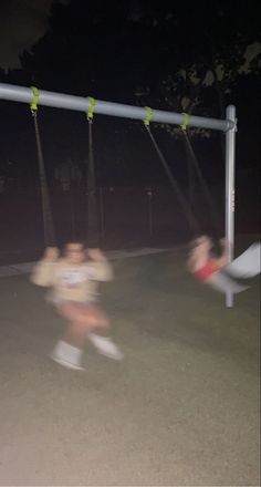 two people are playing on a swing set in the dark, with one person running towards the camera