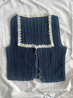 a blue knitted sweater with white trim on top of a bed covered in sheets