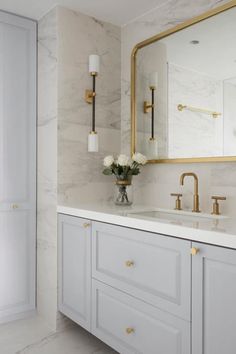 a white bathroom with marble counter tops and gold accents