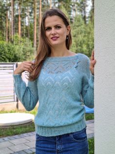 a woman wearing a blue sweater standing next to a white wall with trees in the background