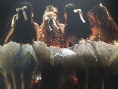 four women dressed in white tutus and bows are talking to each other on stage