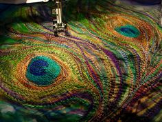 the sewing machine is next to an intricately designed piece of fabric that looks like a peacock's tail