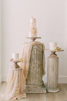 two cakes on top of pedestals in front of a white wall and wooden floor