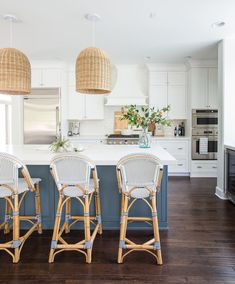 three wicker bar stools sit in the middle of a kitchen with white cabinets