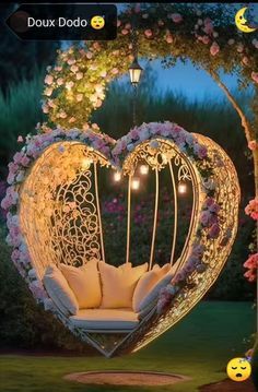 a heart shaped swing chair in the middle of a garden with flowers and lights around it