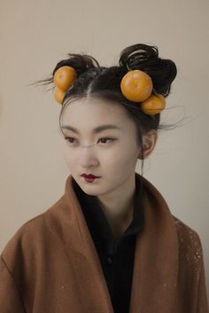 a woman with oranges on her head and hair in buns, looking at the camera