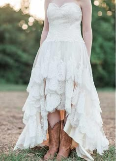 a woman wearing cowboy boots standing in the grass with her dress flowing over her body