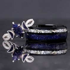 two rings with blue and white diamonds on them sitting next to each other in front of a reflective surface