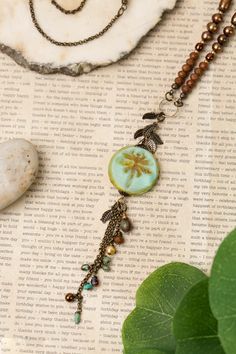 a close up of a necklace on top of a piece of paper next to a leaf