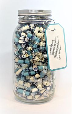 a glass jar filled with lots of different types of beads and wires next to a tag