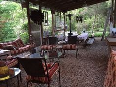 an outdoor covered patio with chairs, tables and couches on gravel ground next to trees