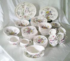 a table topped with lots of white plates and bowls covered in floral designs on top of a white cloth