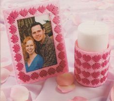 a photo frame next to a candle on a bed of pink flowers with petals around it