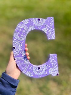 a person holding up a purple letter with white designs on it's sides and the letter c in the middle