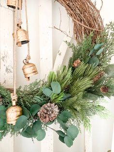 a wreath with evergreen, pine cones and bells hanging from the side of a wall