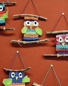 four colorful owls made out of yarn hanging from clothes pins on a red wall with sticks attached to them