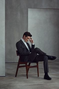 a man in a suit sitting on a chair with his foot up to his face